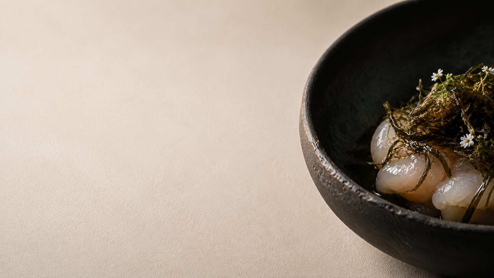 The first movement: shellfish and sea herbs in a dark stone bowl